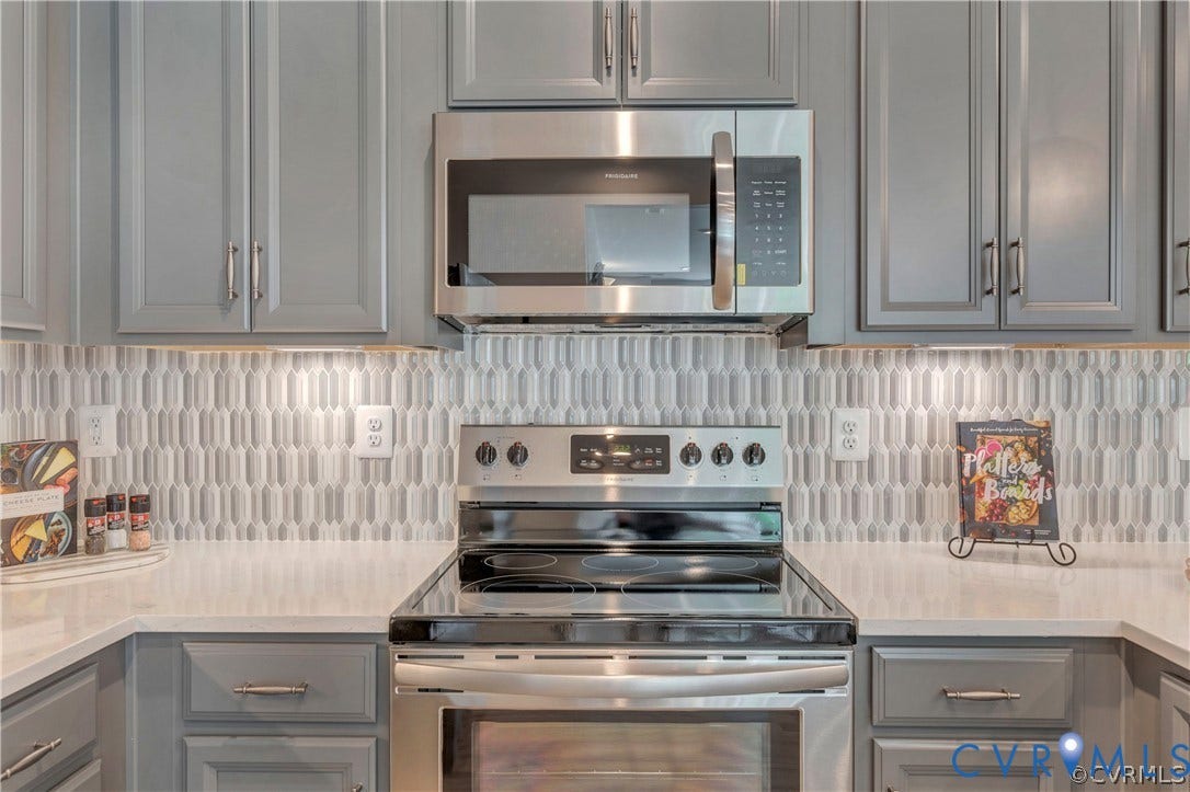 Shaker-style cabinetry, stainless steel microwave, glass-top range, quartz countertops, and a decorative picket-pattern tile backsplash