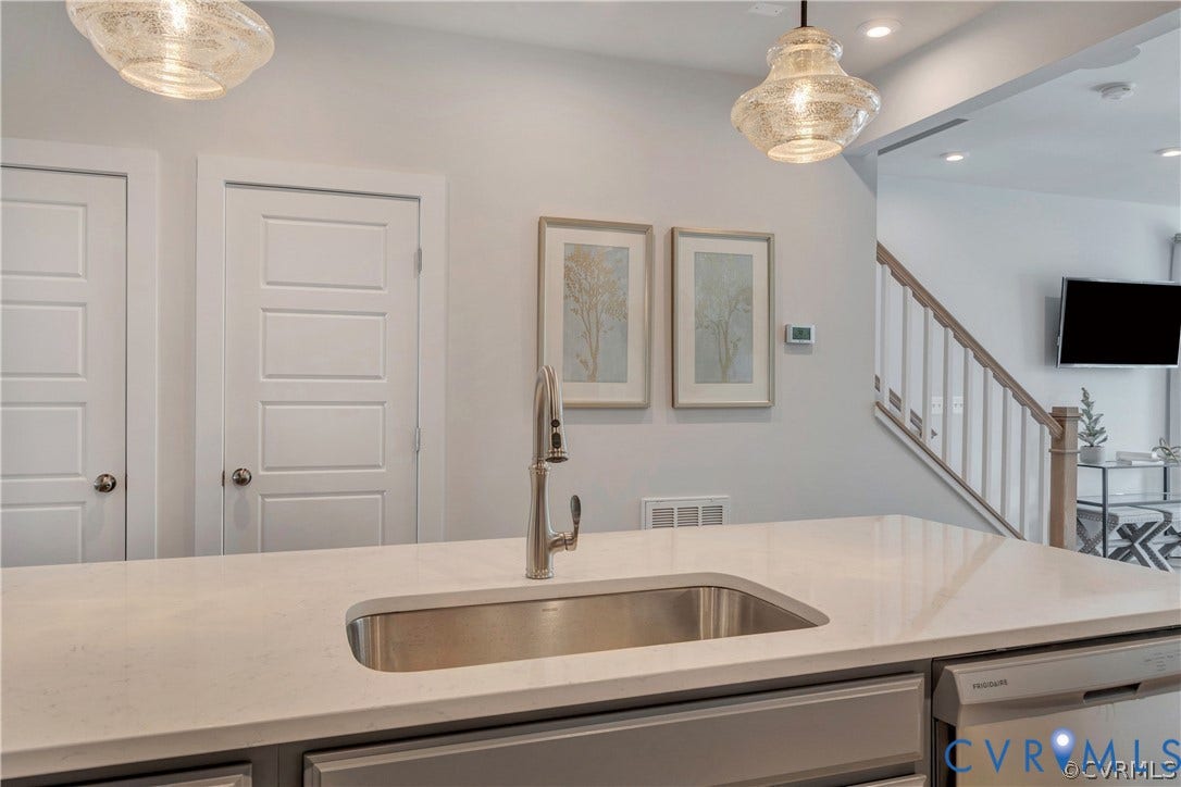 Kitchen island featuring a solid-surface countertop, under-mount stainless steel sink, gooseneck pull-down faucet, and decorative pendant lighting