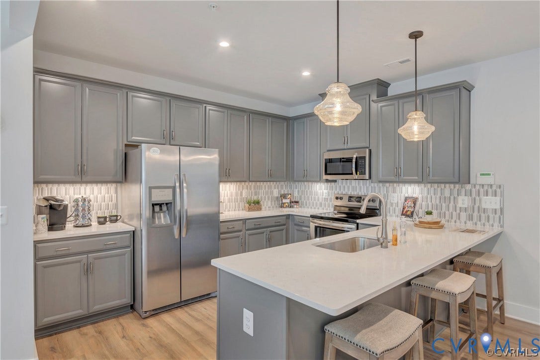 Kitchen featuring shaker-style grey cabinetry, quartz countertops, a stone-patterned tile backsplash, stainless steel appliances, and pendant lighting