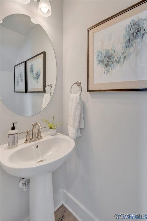 Oval wall-mounted mirror, white pedestal sink, brushed nickel widespread faucet, and ring-style towel holder
