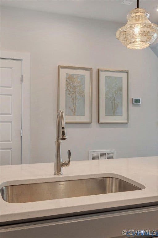 Undermount stainless steel kitchen sink featuring a high-arc pull-down faucet, set within a solid-surface countertop and complemented by a textured glass pendant light fixture