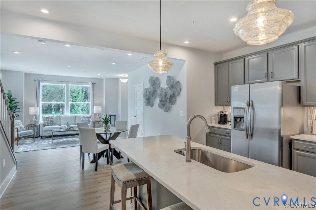 Kitchen island with quartz countertop and stainless steel under-mount sink, complemented by shaker-style cabinetry and multi-light pendant fixtures