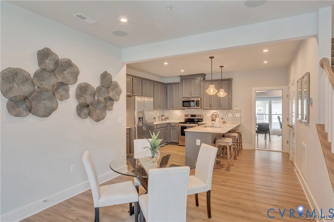 Kitchen featuring grey cabinetry, stone-finish countertops, stainless steel appliances, a central island with bar seating, and wood-finish flooring