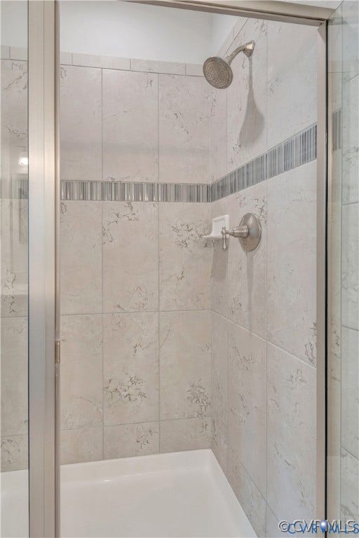 Walk-in shower featuring large-format stone-pattern tile, decorative mosaic accent banding, built-in soap niche, and brushed nickel fixture
