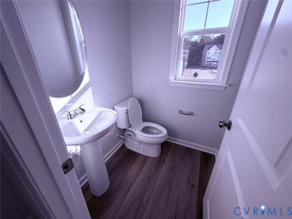 504 Sybil Street, Glen Allen, VA 23060 Pedestal sink with polished chrome faucet, wood-finish flooring, dual-flush toilet, oval wall-mounted mirror, and multi-pane window
