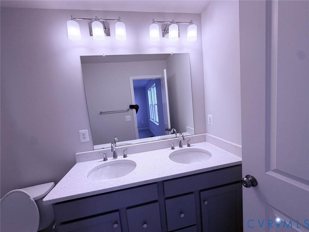 504 Sybil Street, Glen Allen, VA 23060 Dual-sink vanity with solid-surface countertop, cabinetry with brushed-metal hardware, large wall-mounted mirror, and multi-bulb polished-chrome vanity lighting