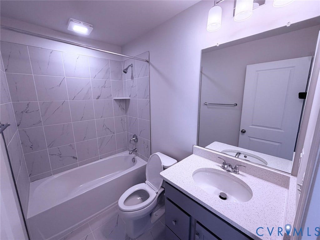 504 Sybil Street, Glen Allen, VA 23060 Bathroom featuring a tub-shower combination with floor-to-ceiling tile surround, a vanity with a quartz countertop, an integrated oval sink, and a large frameless mirror