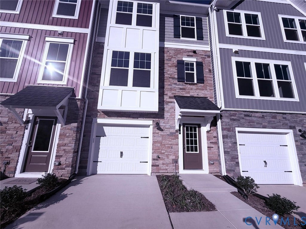 504 Sybil Street, Glen Allen, VA 23060 Multi-story townhouse exterior featuring mixed-material facade of stone veneer and vertical siding, covered entryways, attached garage with carriage-style doors, and multi-pane windows with shutters