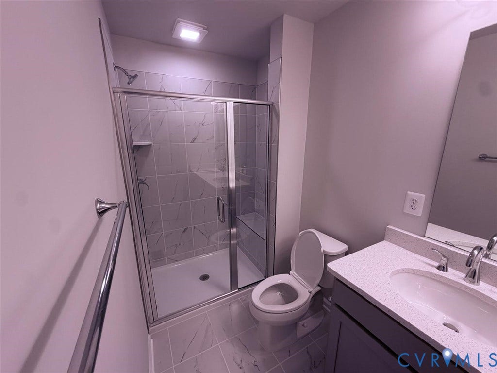 504 Sybil Street, Glen Allen, VA 23060 Bathroom featuring a shower with a chrome-framed glass enclosure, stone-finish tile surround, vanity with a light-toned quartz countertop, and large-format porcelain tile flooring