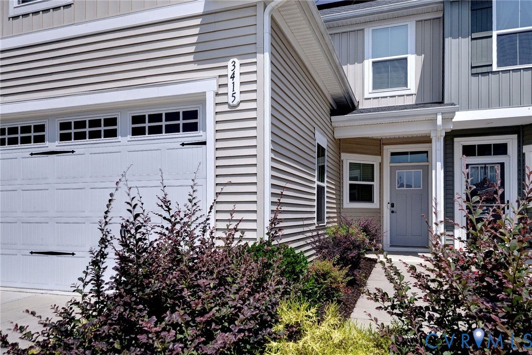 3415 Foxglove Drive, Toano, VA 23168 Exterior featuring light-colored horizontal siding, contrasting vertical siding accents, a panelled garage door with decorative hardware, and a covered entry with a glass-inset door