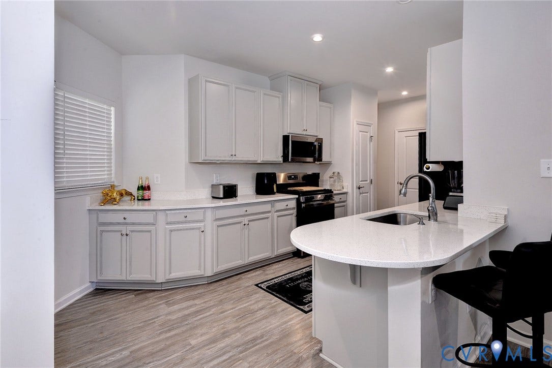 3415 Foxglove Drive, Toano, VA 23168 Kitchen featuring white cabinetry, solid surface countertops, a curved peninsula, stainless steel undermount sink, and wood-finish flooring