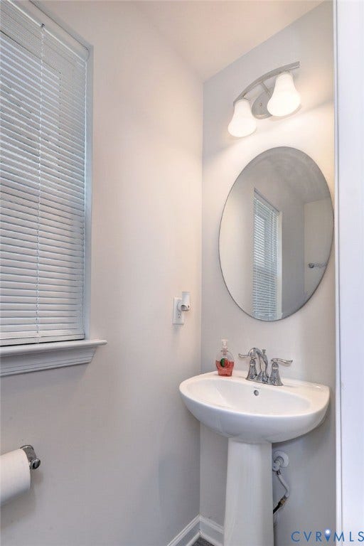 3415 Foxglove Drive, Toano, VA 23168 White pedestal sink with a polished chrome dual-handle faucet, oval wall-mounted mirror, and dual-shade vanity light fixture