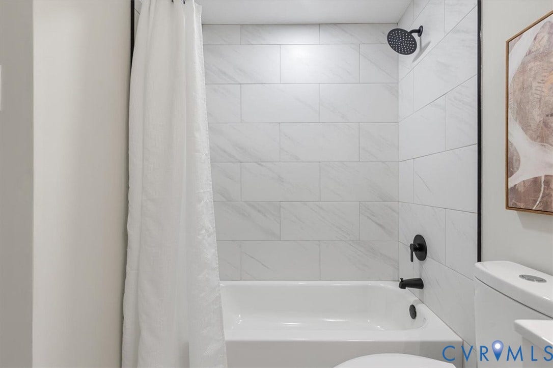 9201 Packard Court, Glen Allen, VA 23060 Full-height shower surround featuring large-format rectangular white tile with subtle veining, matte black rain-style shower head, matching matte black faucet and diverter, and a white soaking tub