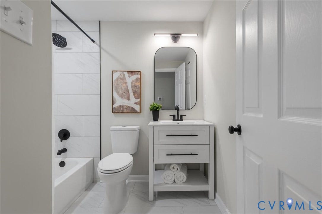 9201 Packard Court, Glen Allen, VA 23060 Bathroom featuring a white vanity with two drawers, an arched mirror, matte black fixtures, and a tub enclosure with large-format tile surround