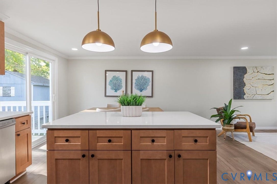 9201 Packard Court, Glen Allen, VA 23060 Kitchen island with light-toned countertop and wood-finish cabinetry, paired with dual metallic pendant lighting, wood-finish flooring, and sliding glass door