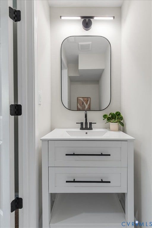 9201 Packard Court, Glen Allen, VA 23060 White vanity featuring two storage drawers, matte black hardware, a rectangular sink, and a white countertop, complemented by a black-framed rounded mirror, a linear wall-mounted light fixture, and a widespread matte black faucet