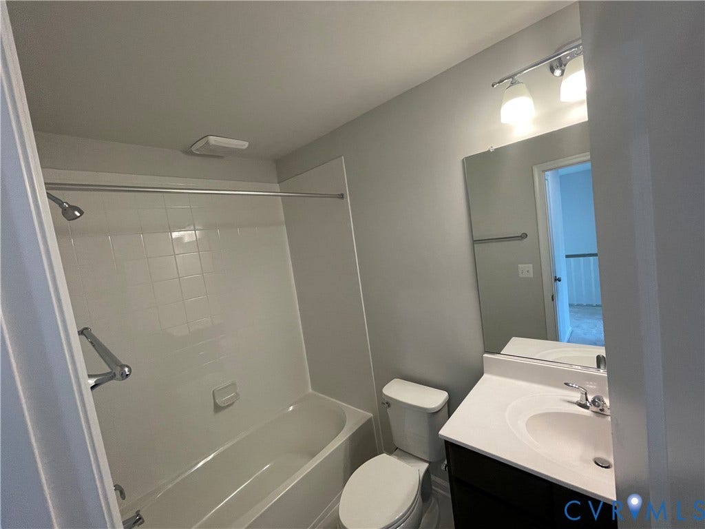 9212 St Charles Circle, Richmond, VA 23235 Bathroom featuring a tub-shower combination with white tile surround, vanity with an integrated countertop sink, wall-mounted mirror, and polished metal hardware