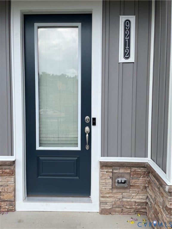 9212 St Charles Circle, Richmond, VA 23235 Entryway featuring a dark-finish door with an integrated glass panel, vertical panel siding, stone veneer wainscoting, and a vertical address plaque