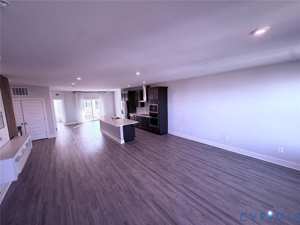 4411 GREYBULL Walk, #B, Glen Allen, VA 23233 Open-concept kitchen featuring dark cabinetry, a central island with a light-toned countertop, built-in stainless steel appliances, and wood-finish flooring