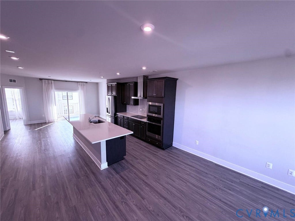 4411 GREYBULL Walk, #B, Glen Allen, VA 23233 Kitchen featuring dark cabinetry, expansive stone-surface island with integrated sink, stainless steel built-in double wall oven, and wood-finish flooring throughout
