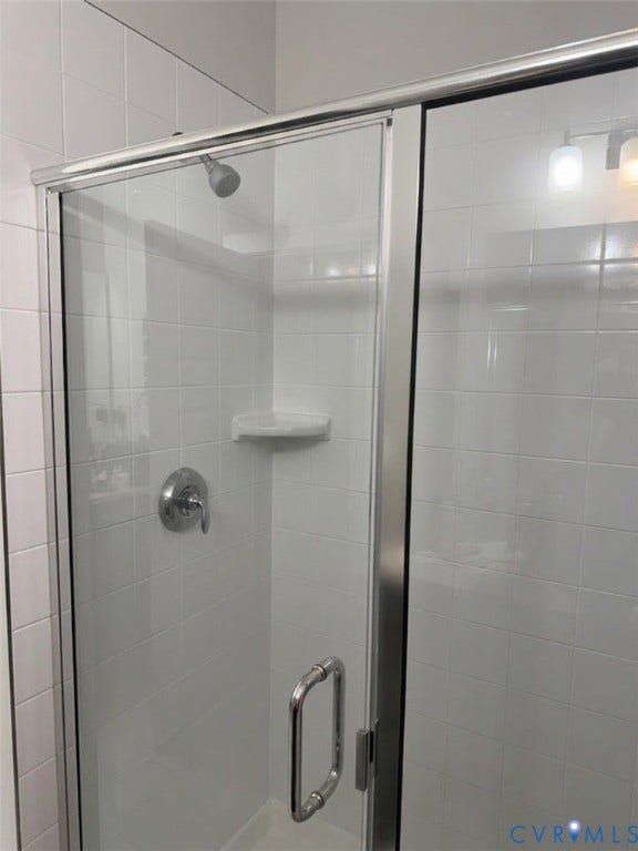 4411 GREYBULL Walk, #B, Glen Allen, VA 23233 Walk-in shower featuring white wall tile, a glass door with a polished metal frame, built-in corner shelving, and a single-handle faucet