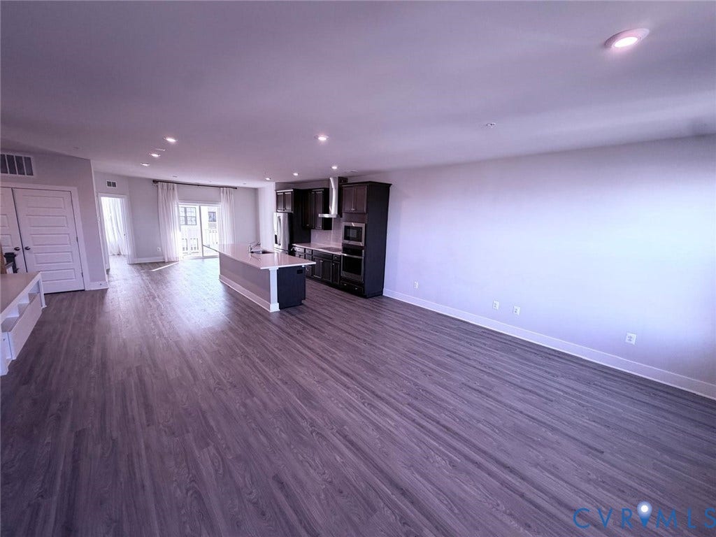 4411 GREYBULL Walk, #B, Glen Allen, VA 23233 Open-concept interior featuring wood-finish flooring, recessed lighting, and a kitchen equipped with dark-toned cabinetry, an island with countertop seating, and a stainless steel range hood