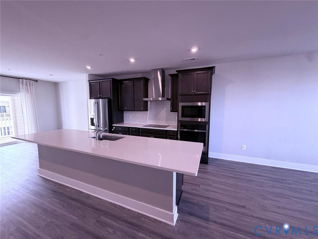 4411 GREYBULL Walk, #B, Glen Allen, VA 23233 Kitchen featuring a central island with a solid surface countertop and undermount sink, dark-toned cabinetry, stainless steel appliances, recessed lighting, and wood-finish flooring
