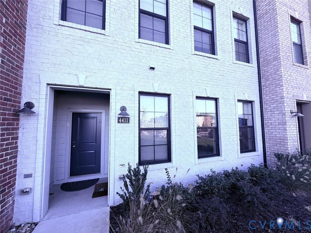 4411 GREYBULL Walk, #B, Glen Allen, VA 23233 Exterior facade featuring painted brick masonry, grid-pane windows with dark frames, recessed entry, and wall-mounted exterior lighting