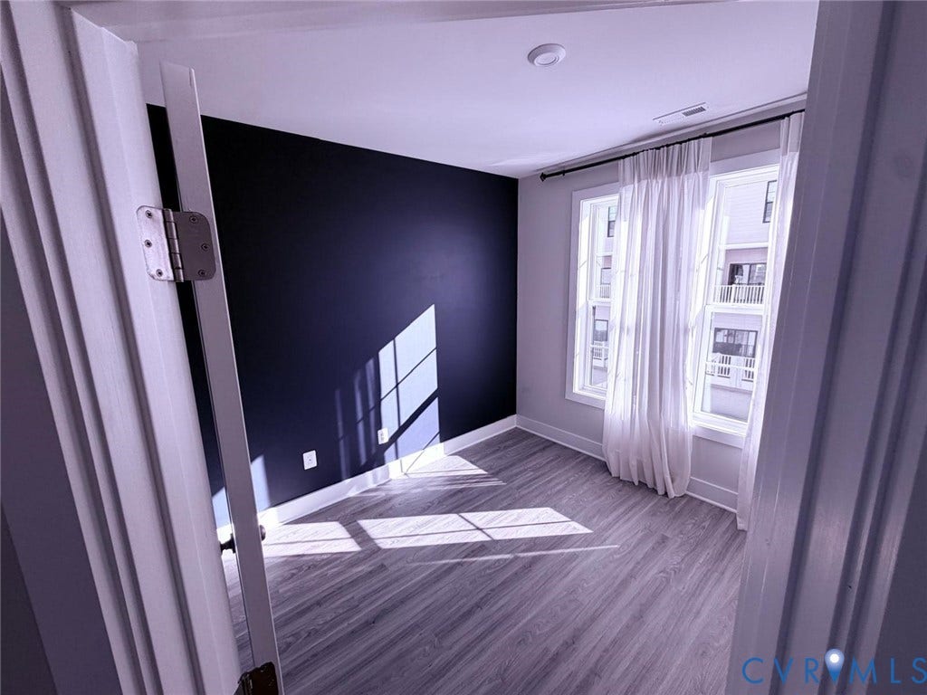 4411 GREYBULL Walk, #B, Glen Allen, VA 23233 Room featuring wood-finish flooring, a charcoal accent wall, and dual windows with window casing