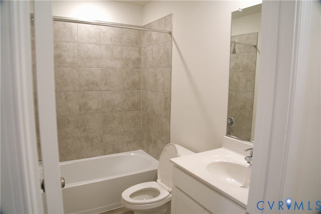 16005 Abelson Way, Chesterfield, VA 23832 Bathroom featuring a white vanity with a composite countertop and integrated sink, a full-height wall-mounted mirror, and a tub with a surround of neutral-toned square tile