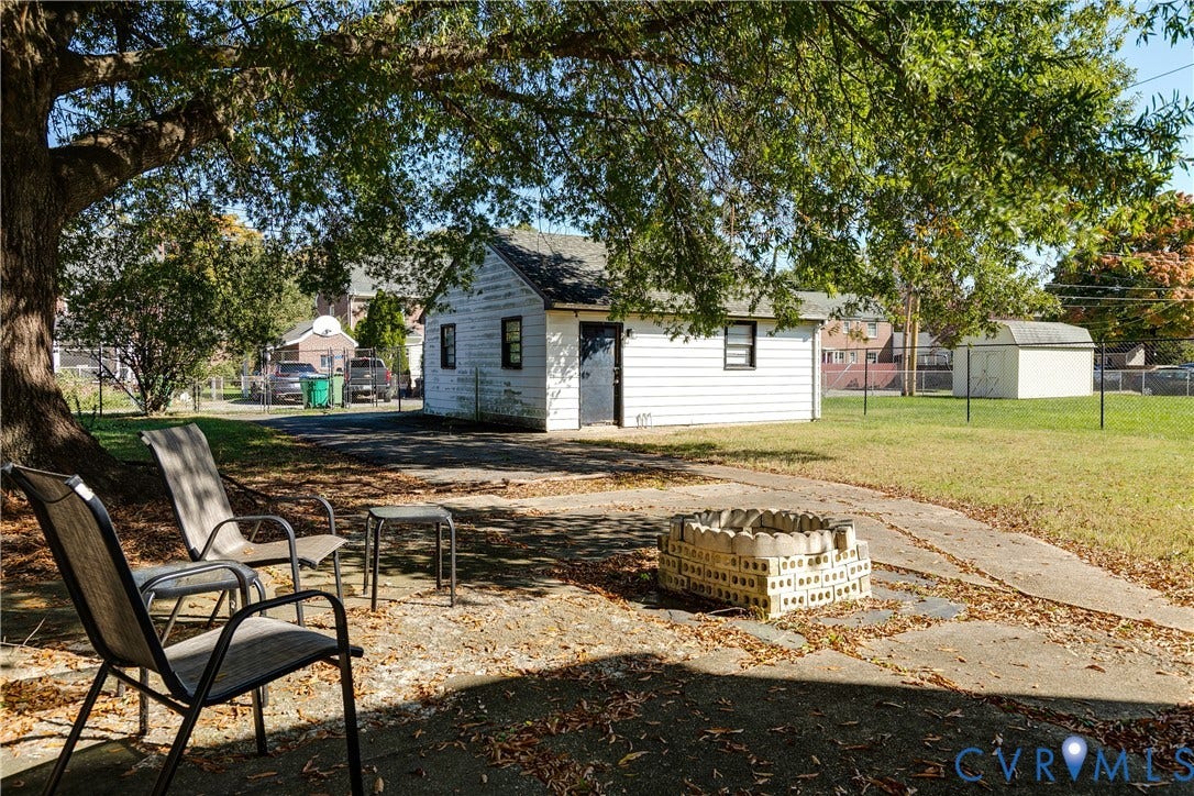 1406 Wentbridge Road, Richmond, VA 23227 Concrete patio featuring a masonry fire pit, mature shade tree, detached structure with exterior siding, and fenced yard