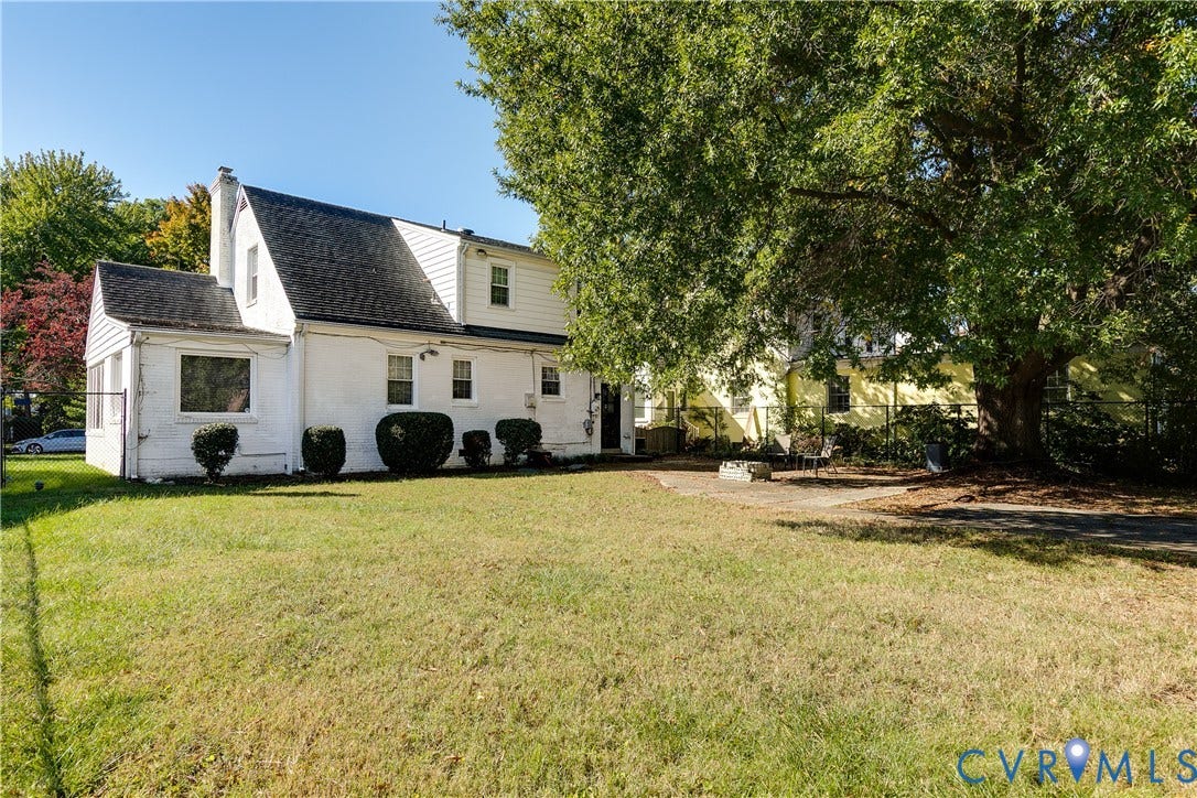 1406 Wentbridge Road, Richmond, VA 23227 White exterior residence featuring a steeply pitched roofline, exterior brick construction, a rear patio area, and mature trees on the grounds