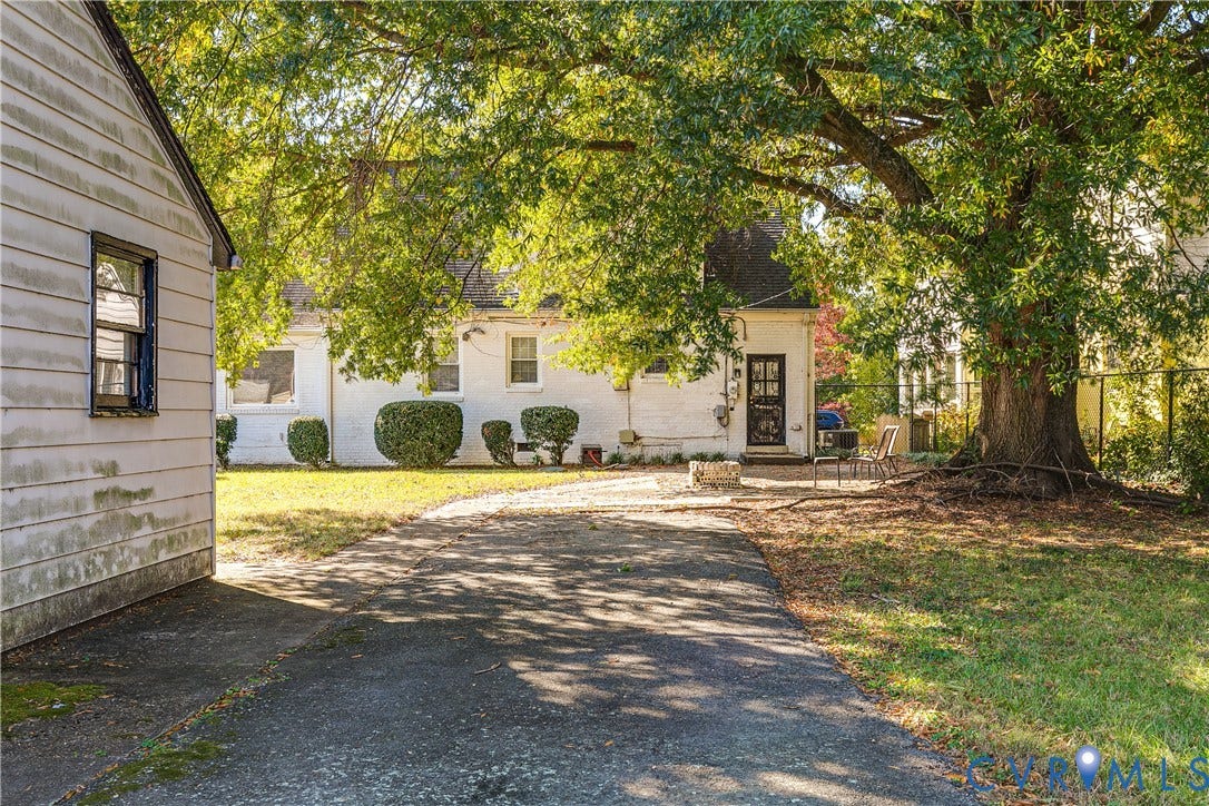 1406 Wentbridge Road, Richmond, VA 23227 White-painted brick exterior featuring a multi-pane glass door, paved driveway, stone fire pit, and mature shade tree