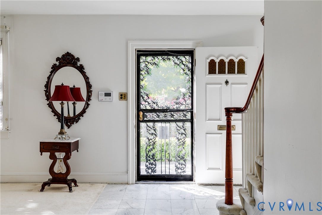 1406 Wentbridge Road, Richmond, VA 23227 Entryway featuring a white paneled front door with decorative transom window, black metal screen door, stone-finish flooring, and a wooden staircase with a polished banister