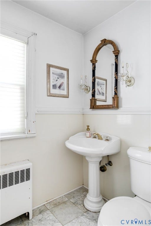 1406 Wentbridge Road, Richmond, VA 23227 Pedestal sink with brass-finish hardware, wall-mounted arched mirror, dual crystal-style wall sconces, and natural stone tile flooring
