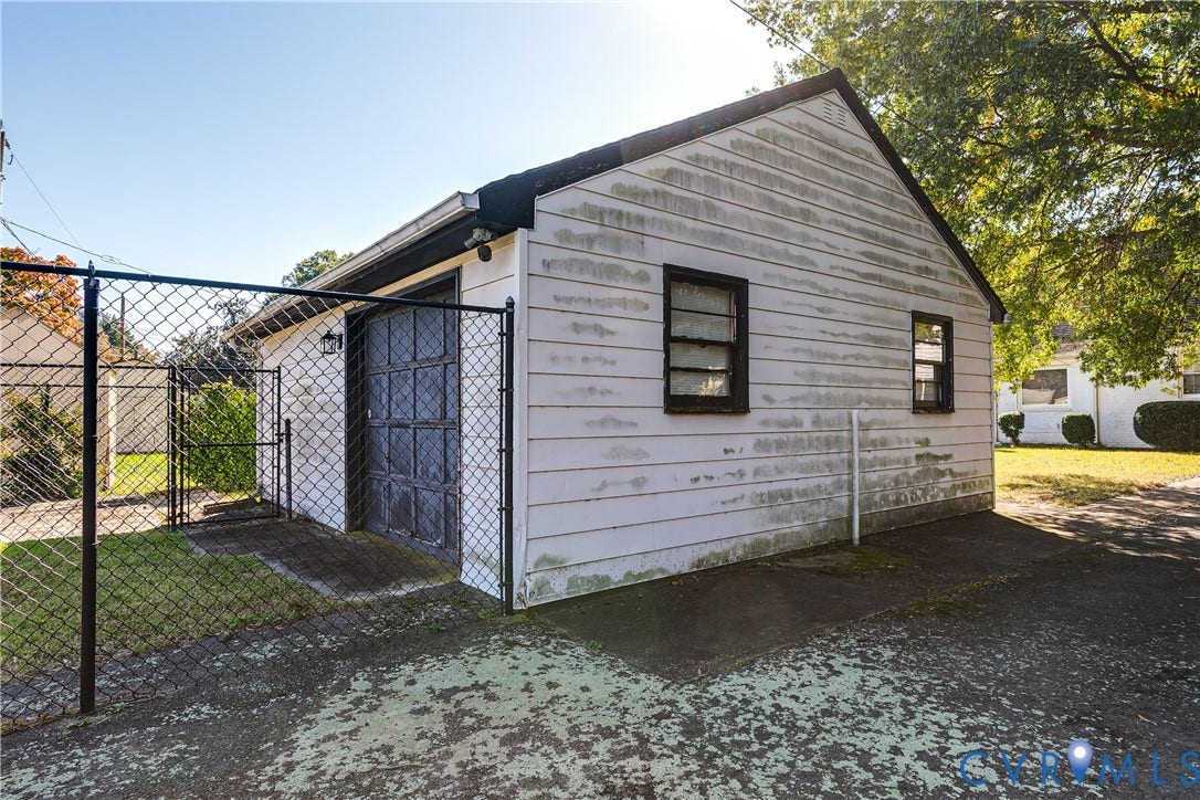 1406 Wentbridge Road, Richmond, VA 23227 Detached garage structure featuring horizontal lap siding, a paneled overhead door, two single-hung windows, and an enclosed chain-link fence perimeter