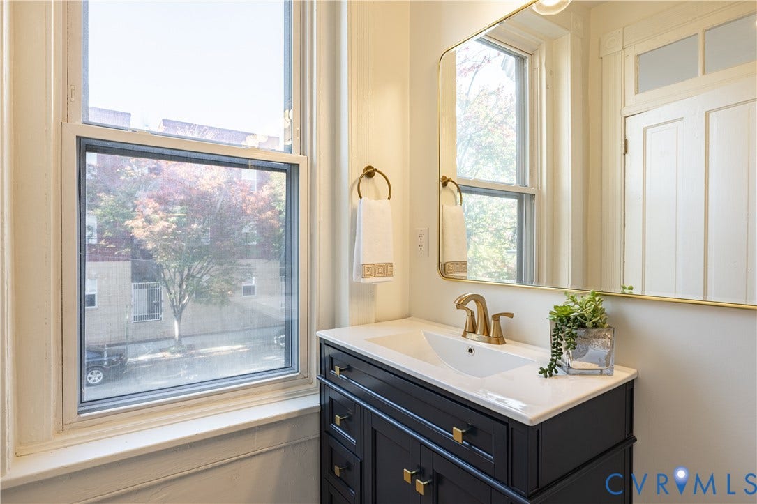 1108 W Marshall Street, Richmond, VA 23220 Dark-finish vanity featuring brass hardware and a white integrated sink, complemented by a gold-trimmed wall mirror, brass-toned faucet, and brass-finish towel ring