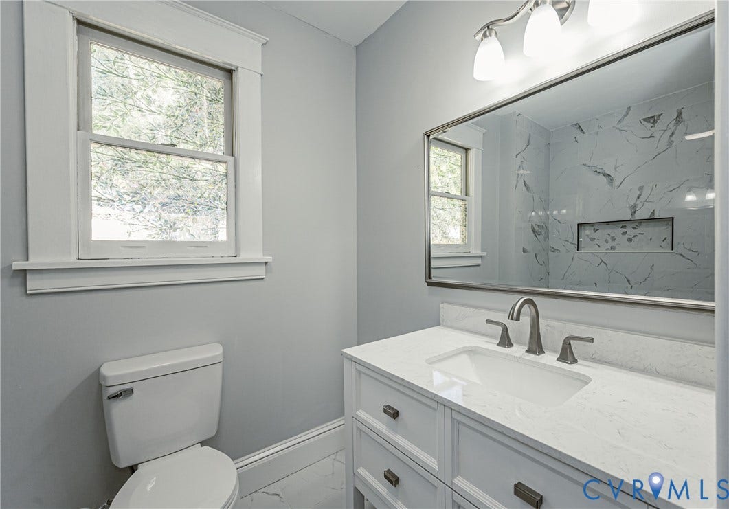 710 La Von Drive, Henrico, VA 23227 Vanity featuring a white countertop with an integrated basin, brushed metal hardware, wall-mounted mirror, and tile-surround shower with a built-in niche