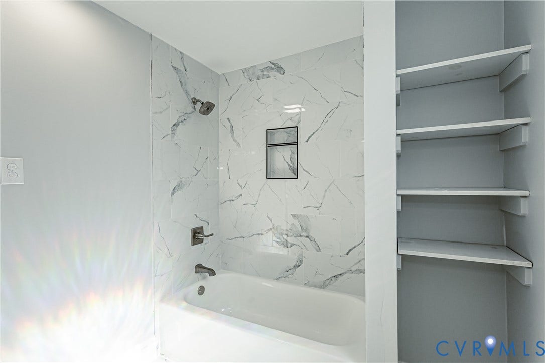 710 La Von Drive, Henrico, VA 23227 Bathtub with a shower head, wall-mounted faucet, built-in recessed wall niche, and stone-finish tile surround, complemented by a dedicated built-in shelving unit