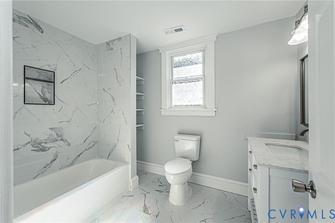 710 La Von Drive, Henrico, VA 23227 Bathroom featuring a vanity with a composite stone countertop, large-format tile flooring, a bathtub surround with floor-to-ceiling tile, built-in shelving, and a wall-mounted light fixture