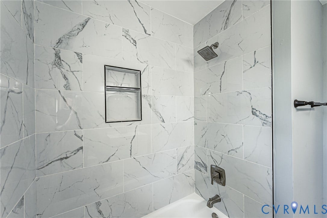 506 Meadowspring Road, Henrico, VA 23223 Bathtub surround featuring large-format white stone-patterned tile, integrated recessed shelving, a metallic shower head, and matching metallic faucet hardware