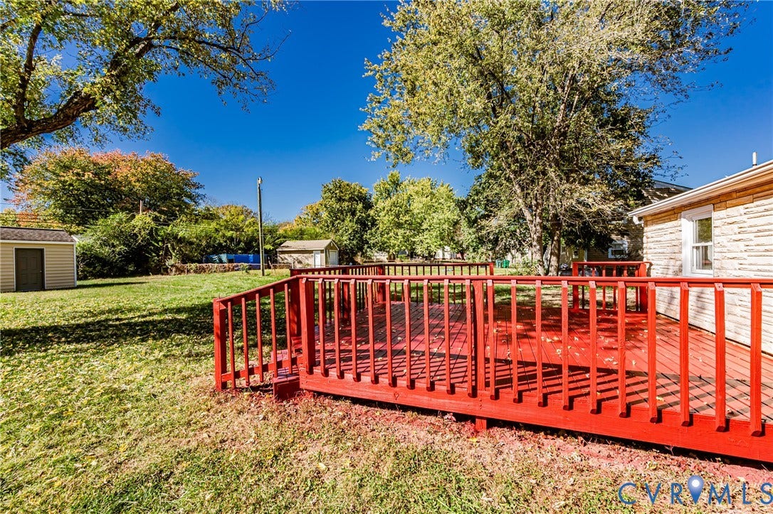 506 Meadowspring Road, Henrico, VA 23223 Backyard featuring a red-painted wood deck, expansive lawn, mature trees, and detached storage structure