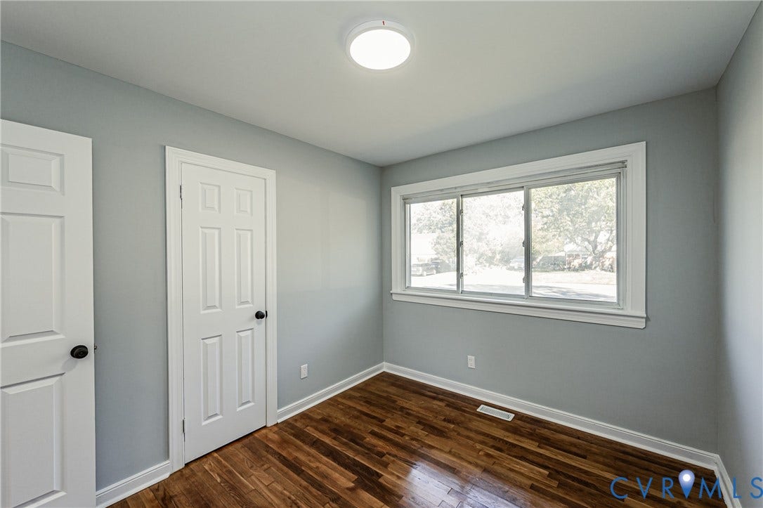 506 Meadowspring Road, Henrico, VA 23223 Room featuring wood-finish flooring, neutral wall paint, two white six-panel doors, a large sliding window, and a central flush-mount ceiling light