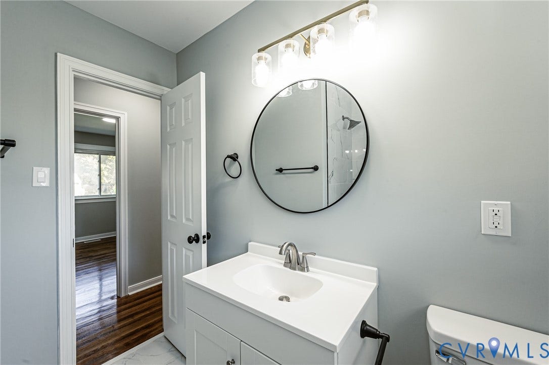 506 Meadowspring Road, Henrico, VA 23223 Bathroom vanity featuring a white cabinet, integrated sink, and polished metal faucet, accented by a circular black-framed mirror, four-light glass fixture, and matte black hardware