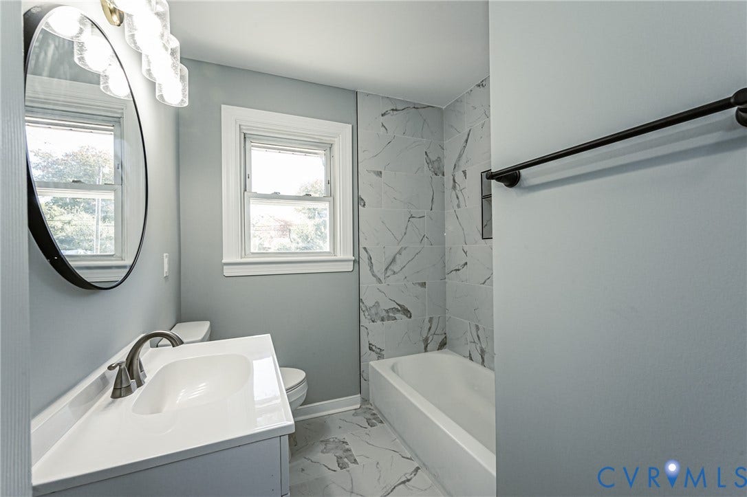 506 Meadowspring Road, Henrico, VA 23223 Bathroom featuring a vanity with an integrated sink and metallic faucet, a round wall-mounted mirror, overhead multi-globe lighting, a shower-tub combination with patterned wall tile, and coordinated floor tile