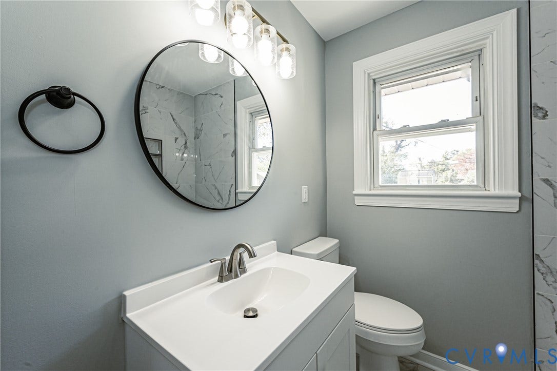 506 Meadowspring Road, Henrico, VA 23223 White vanity cabinet with an integrated basin, sleek metallic faucet, circular wall-mounted mirror, and multi-bulb light fixture