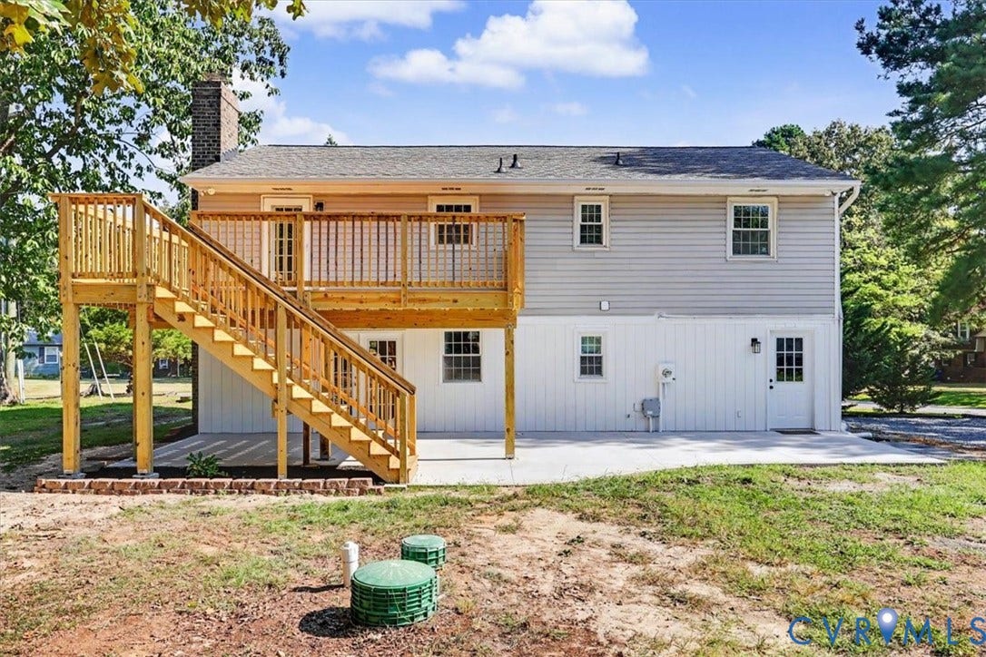 9737 Graves Road, South Chesterfield, VA 23803 Two-story exterior featuring light-toned horizontal siding, a raised wood deck with stair access, a ground-level concrete patio, and a brick chimney