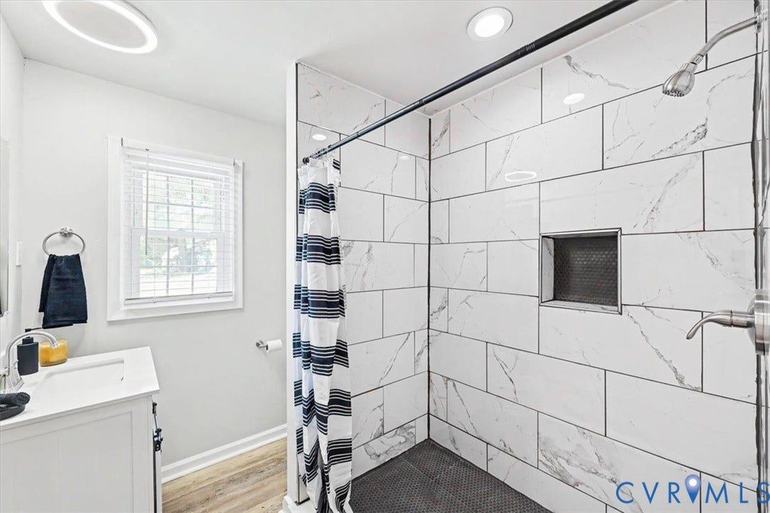 9737 Graves Road, South Chesterfield, VA 23803 Bathroom featuring a shower stall with large-format stone-patterned wall tile, a recessed storage niche, wood-finish flooring, and a white vanity with an integrated basin