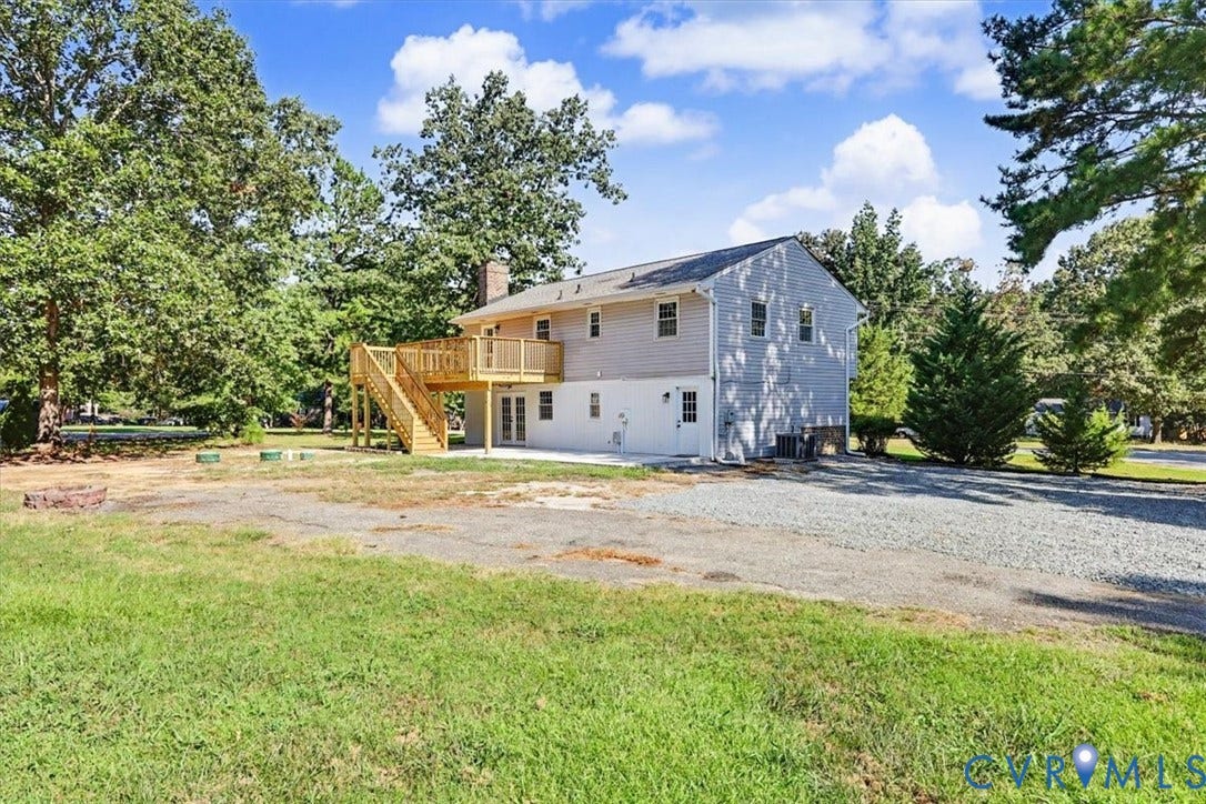 9737 Graves Road, South Chesterfield, VA 23803 Two-story exterior featuring light-toned horizontal siding, a raised wood deck with stair access, a stone chimney, and a gravel driveway