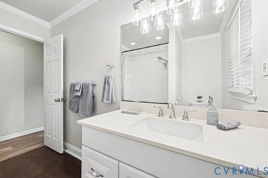 9737 Graves Road, South Chesterfield, VA 23803 Bathroom featuring a white vanity with a composite countertop, undermount sink, multi-light fixture, large wall mirror, and shower with a tub enclosure